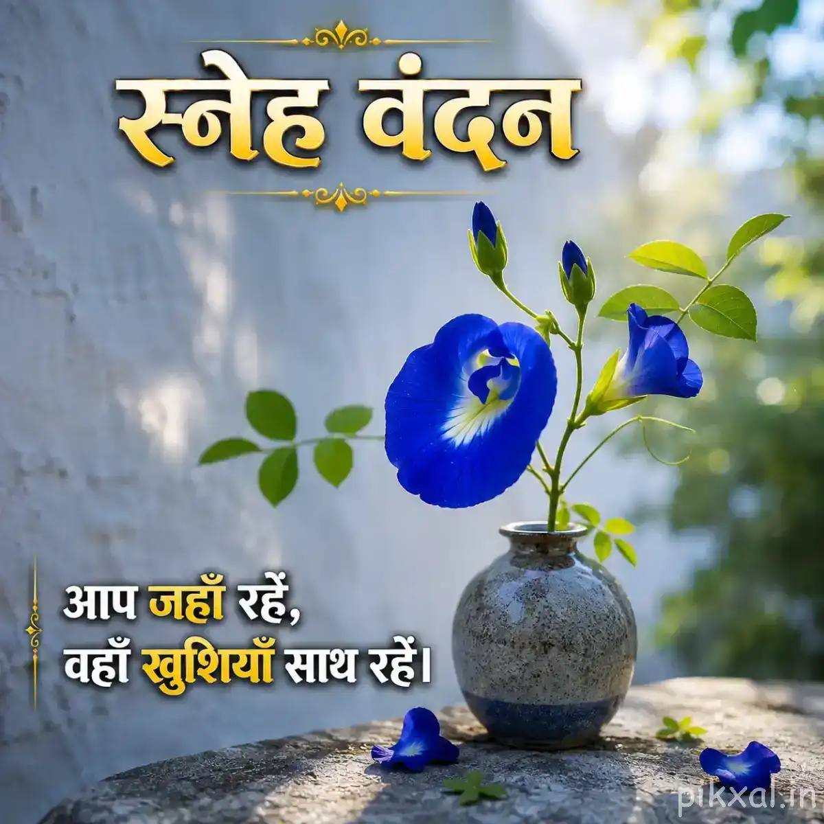 Two blue flowers on a leafy branch in a glass vase with scattered petals and a Hindi morning wish