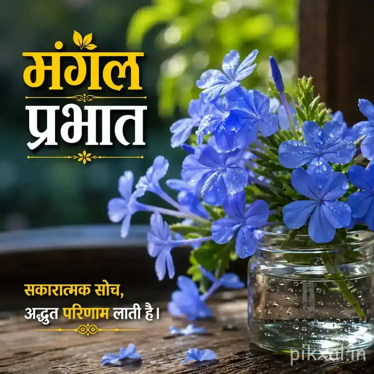 Cluster of blue flowers in a glass jar with green foliage and a Hindi morning greeting